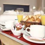 Visuel de l’offre L’Échappée Belle : 1 nuitée à l’Hôtel Antares & Spa Honfleur, montrant une ambiance gourmande avec viennoiseries et boissons.