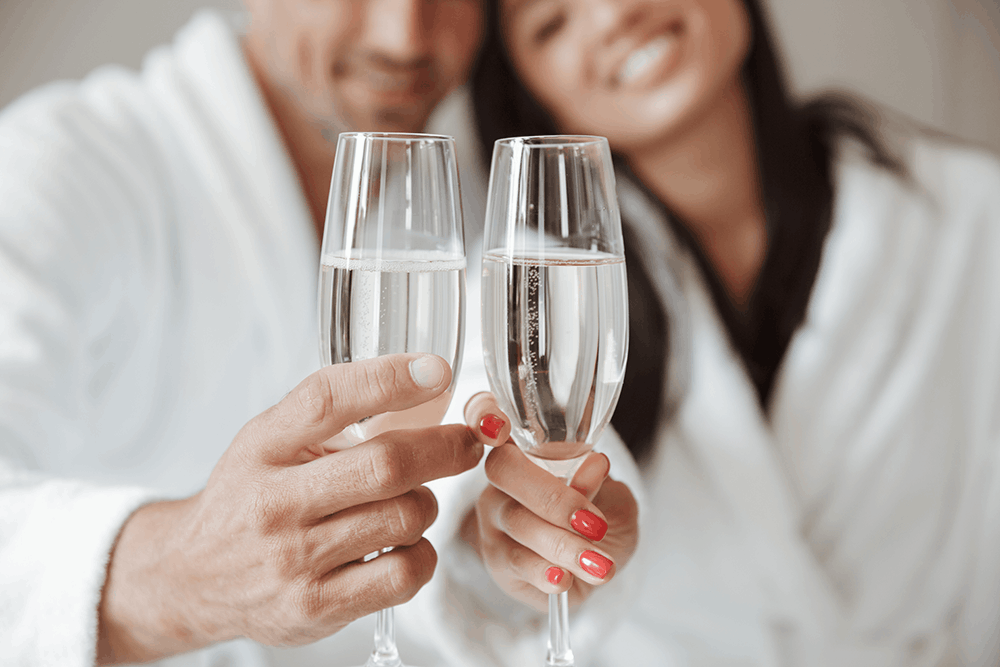 Couple en peignoir trinquant au champagne à l'Hôtel Antares Honfleur – cadeaux et surprises offerts pendant le séjour