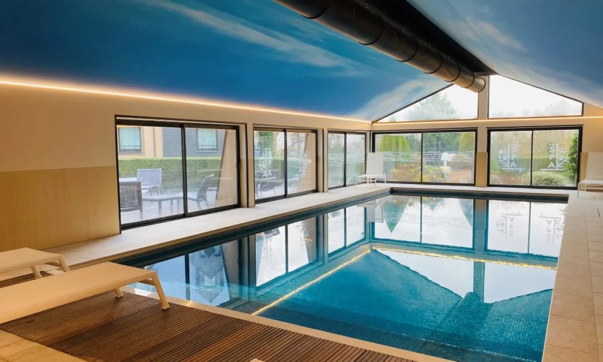 Piscine intérieure avec transats, grandes baies vitrées et plafond bleu à l’Hôtel Antares & Spa Honfleur.